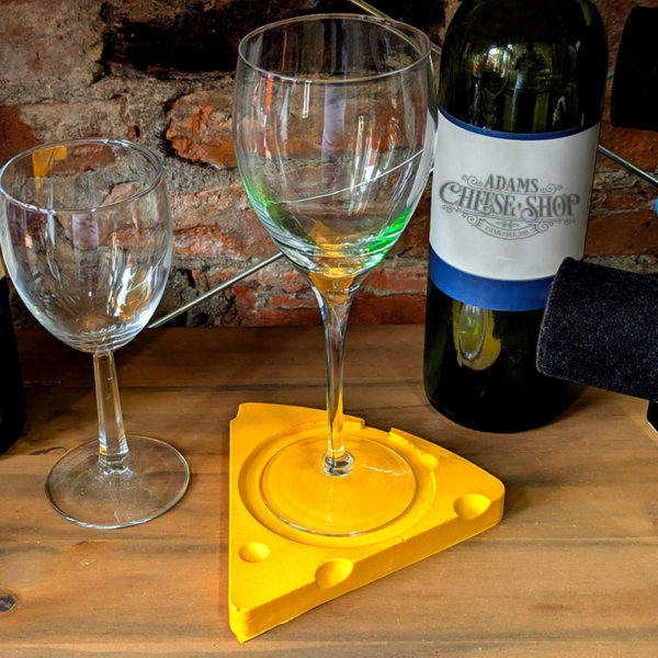 A foam drink coaster shaped like a cheese wedge, with a wine glass sitting on top.