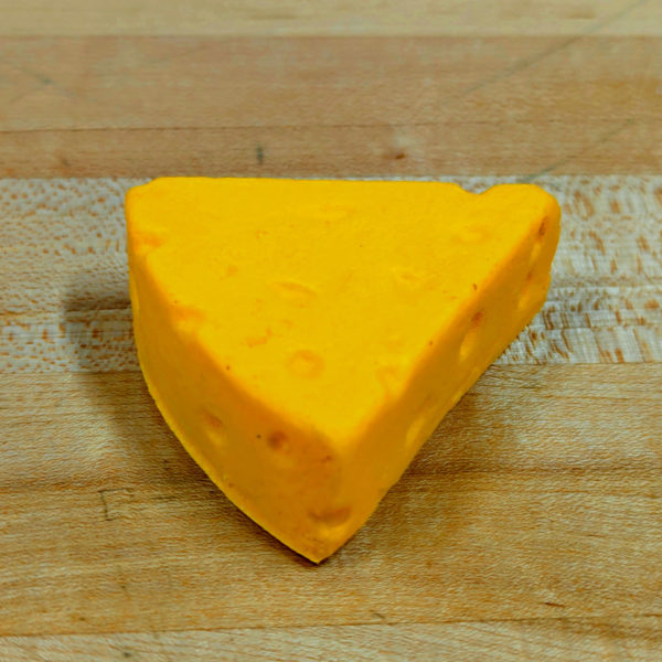 A closeup of a foam magnet shaped like a yellow wedge of cheese, sitting on a wooden counter.