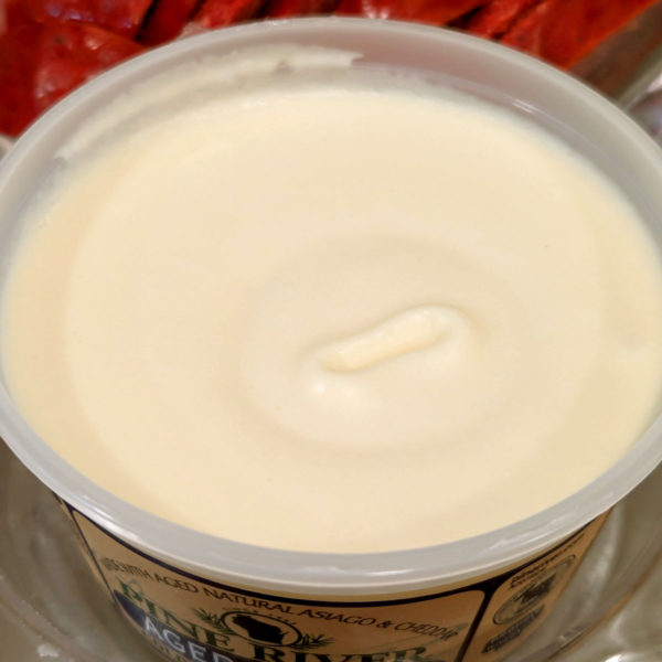 A closeup of Aged Asiago cheese spread in its tub.