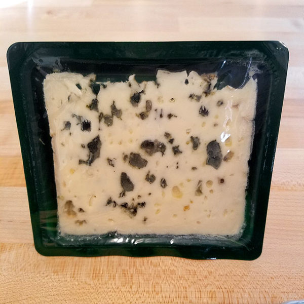 A package of Roquefort cheese with the lid removed, showing the pale paste and mottled green surface.