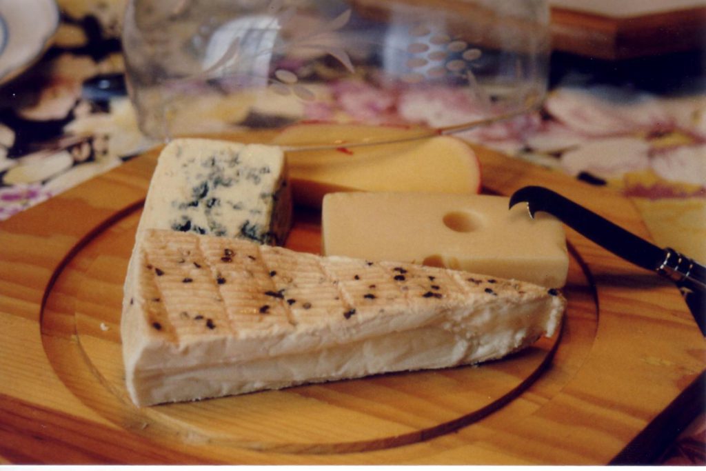 A wooden plate with assorted cheeses on it.