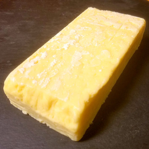 An unwrapped block of Tickler Extra Mature Devonshire Cheddar cheese.