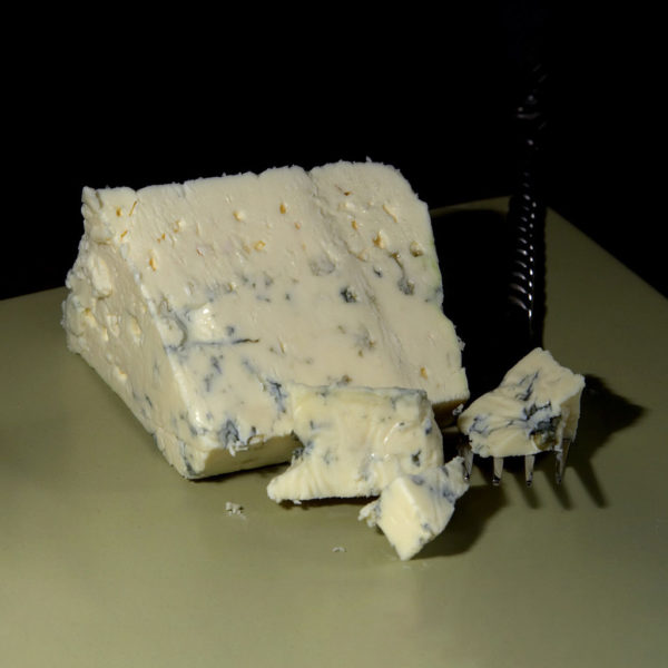 A wedge of Danish Blue cheese being crumbled by a fork.