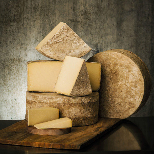 A stack of wheels and wedges of Cabot Clothbound Cheddar cheese.