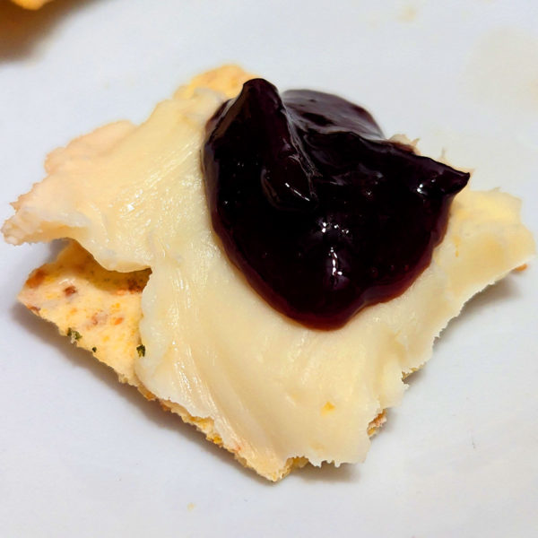 Taleggio spread on a cracker with a black grape and almond accompaniment.