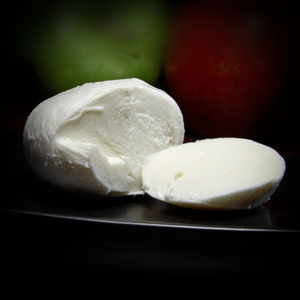 A ball of fresh mozzarella with a chunk sliced off, in front of green and red apples.