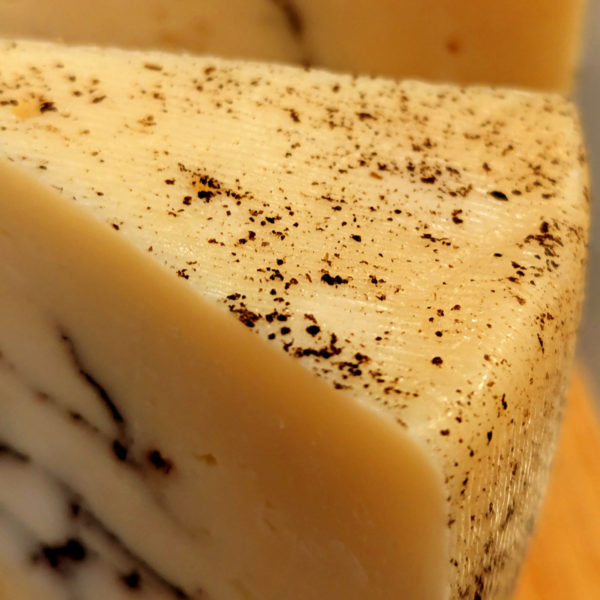 A wedge of The Truffle Kid, with a closeup on the rind speckled with black truffle.