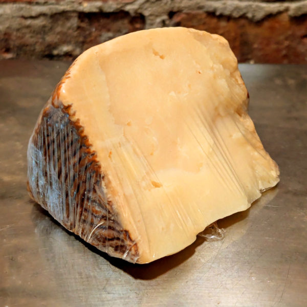 A rustic, cut wedge of Pecorino Calabrese, showing its slight yellow colored paste with large cracks and an uneven surface.