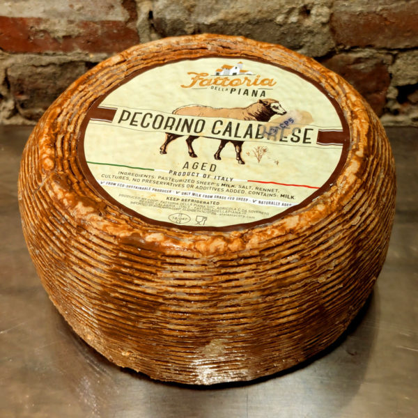 An uncut wheel of Pecorino Calabrese with the label on top, featuring an illustration of a sheep.