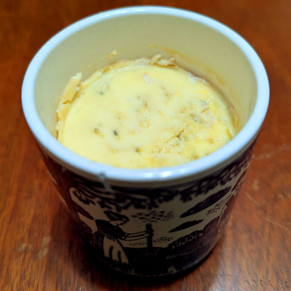 An open ceramic pot of Stilton with the protective wax layer removed, showing the blue cheese inside.