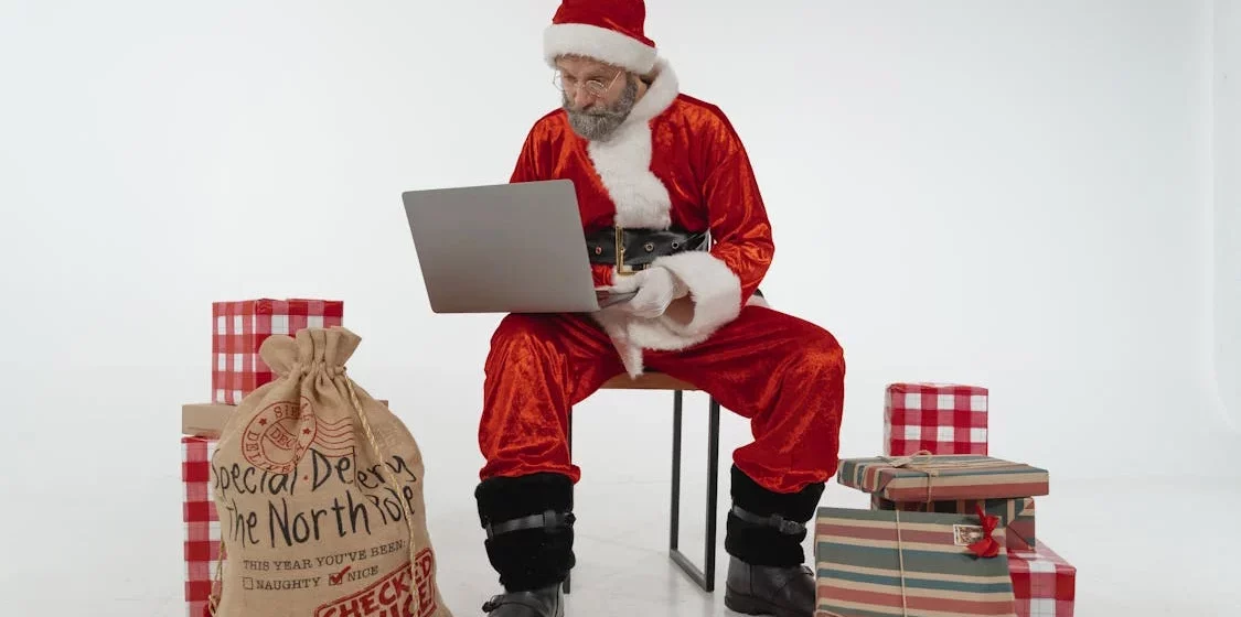 Elderly man in Santa costume, using a laptop.