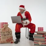 Elderly man in Santa costume, using a laptop.