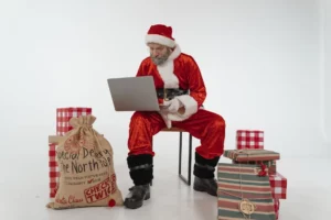 Elderly man in Santa costume, using a laptop.