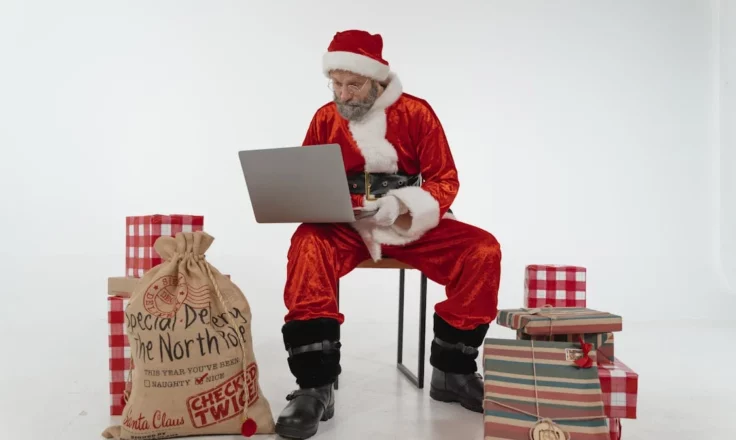 Elderly man in Santa costume, using a laptop.