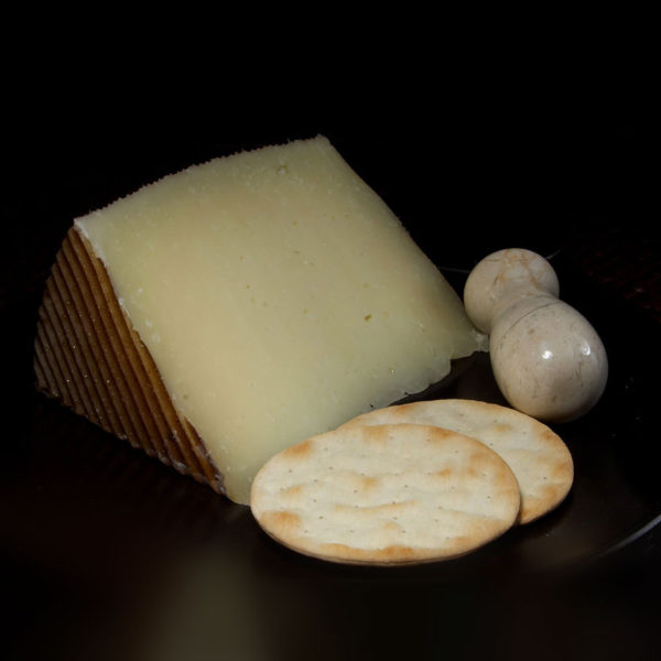 A wedge of Manchego cheese on a plate, with crackers.