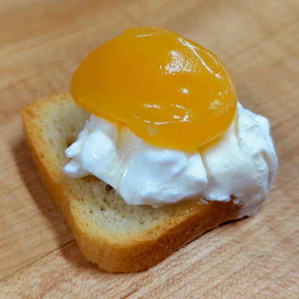 A petit toast with soft white cheese and a dab of lemon curd on top.