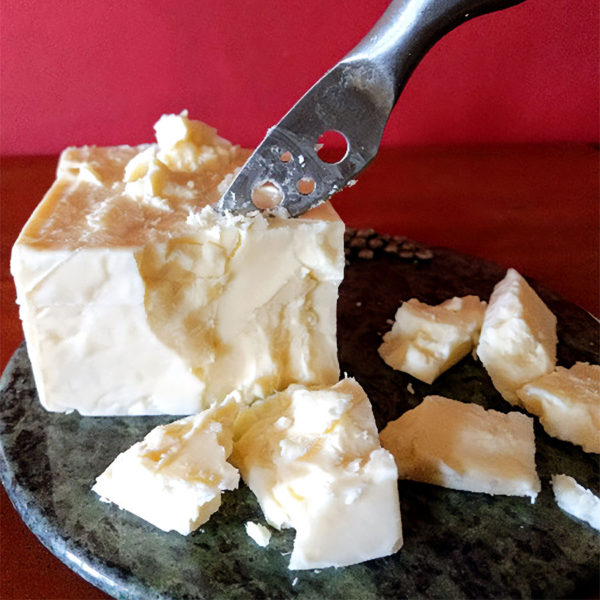 Lake Effect Cheddar cheese on a plate, being crumbled into large chunks by a knife.