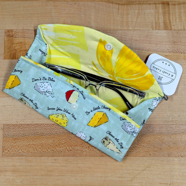 An open glasses case holding a pair of glasses, made from fabric with a cheesy pattern.