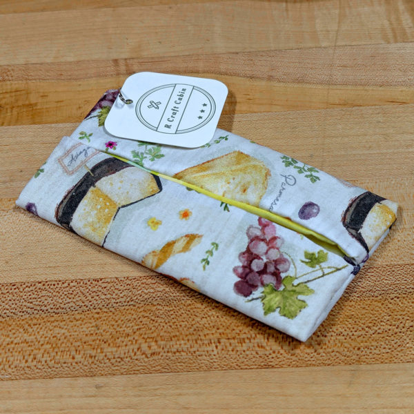 An empty travel tissue holder made from cloth with a cheesy print on the fabic.